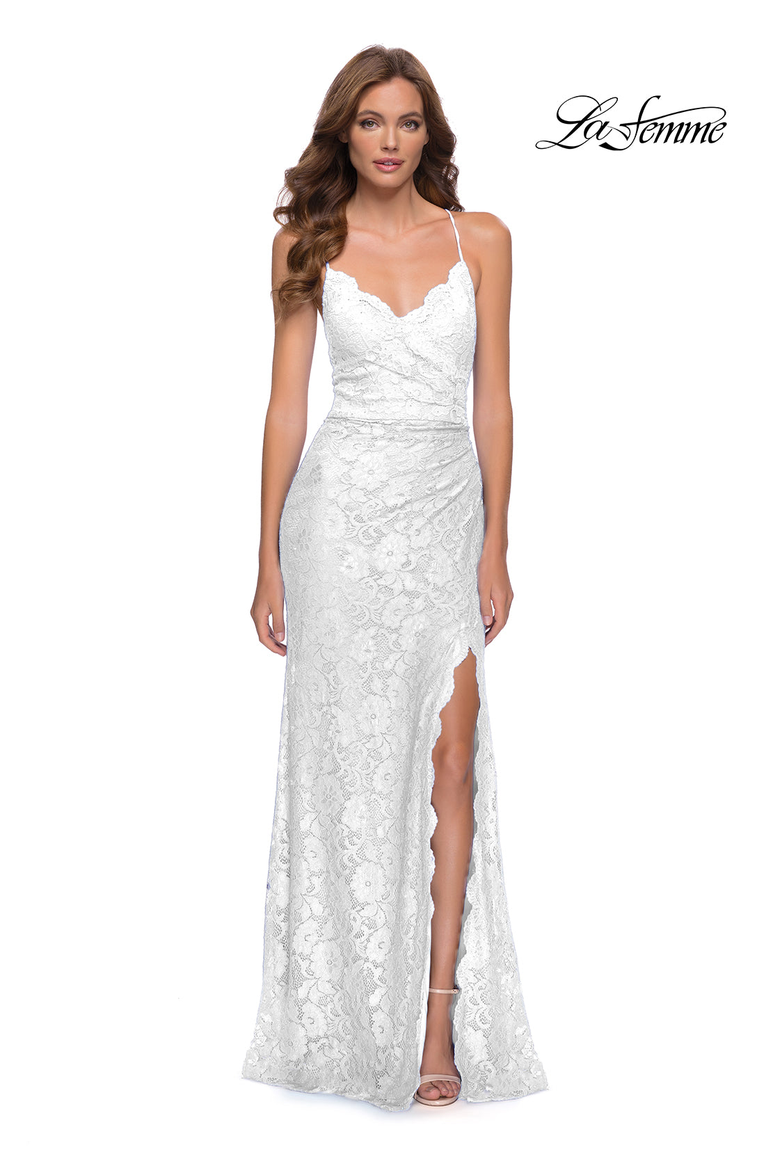A woman wears the Open-Back La Femme Long Lace Prom Dress 29939—a white lace sleeveless gown with a thigh-high slit—as she stands against a plain background. The La Femme logo is in the top right corner.